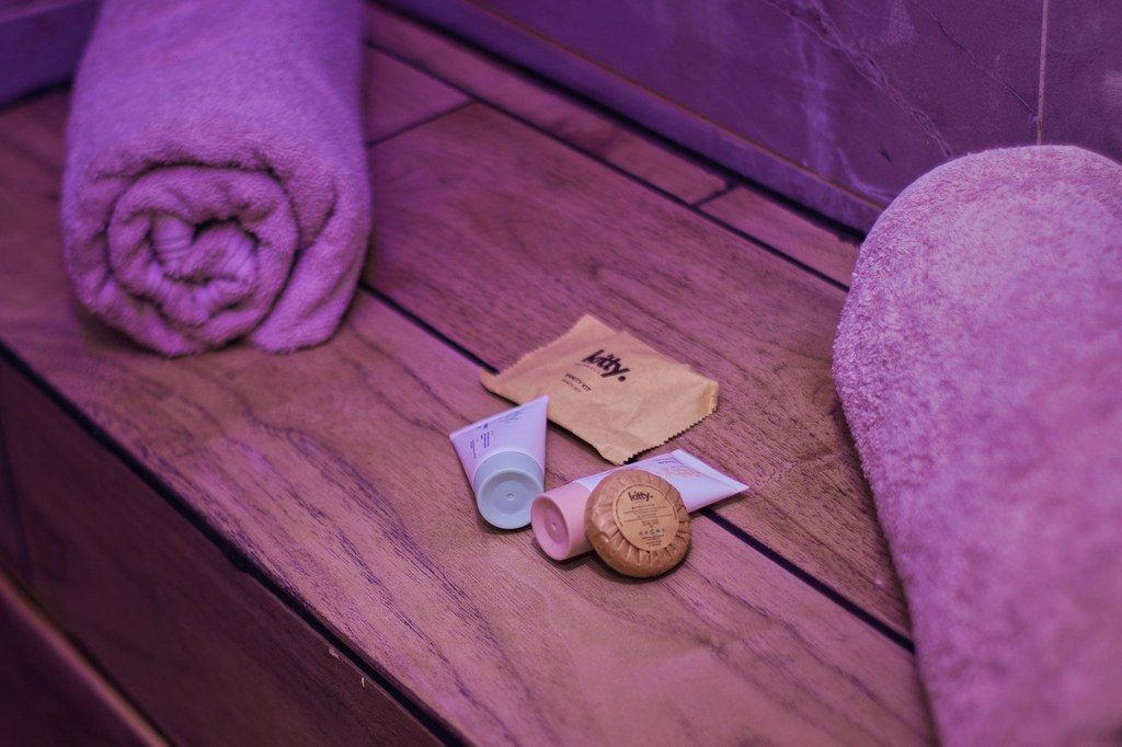 Serviettes roulées et produits d'accueil (savon, gel douche, crème) posés sur le banc en bois