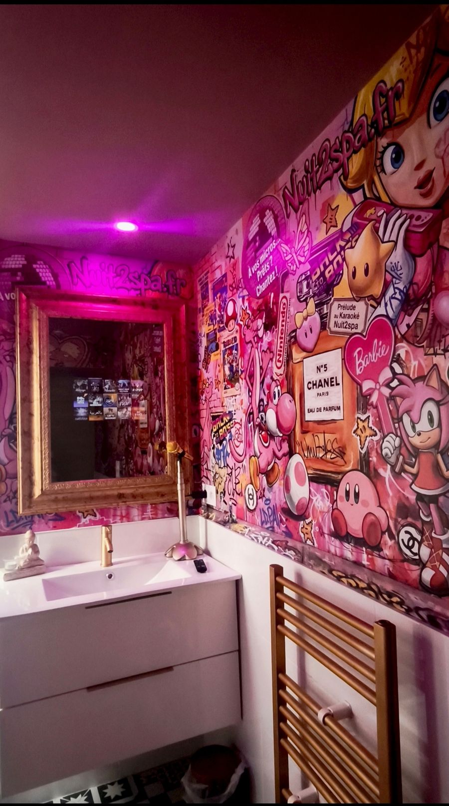Salle d'eau décorée d'une fresque pop rose avec un micro doré près du lavabo